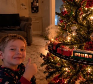 Boy giving a thumbs up next to the Emerald Express on the Christmas tree