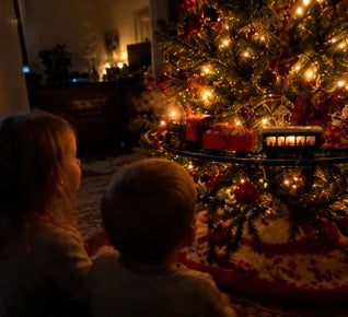 Two children watching the train around a lit tree